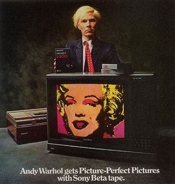 Andy Warhol stands behind a CRT TV holding a Beta tape.
